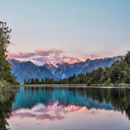 Snow-capped New Zealand mountains reflected in a still lake at sunset