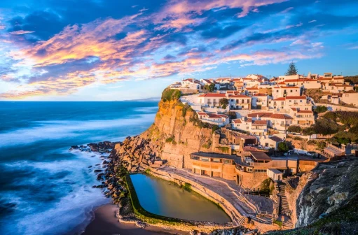 A whitewashed clifftop village above a seawater pool on the Portuguese coast at sunset
